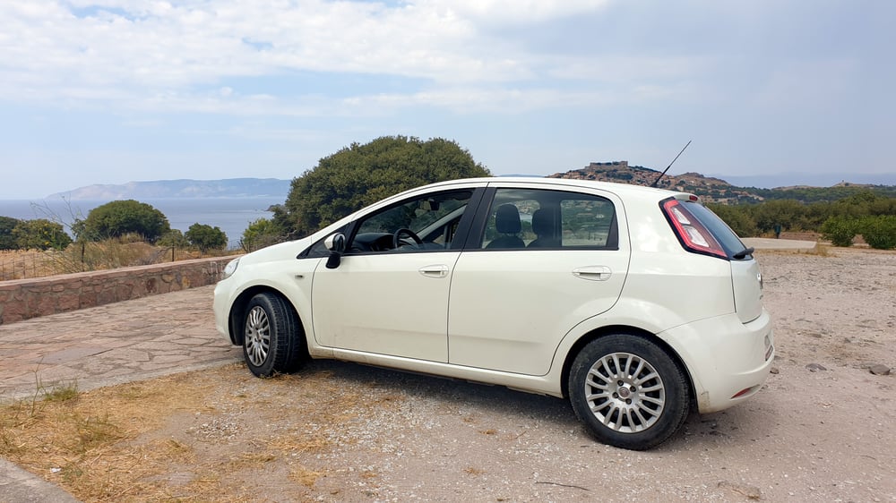 Un'auto bianca parcheggiata con vista sulla costa di Lesbo.